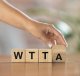 Hand legt houten blokjes met de letters WTTA op tafel