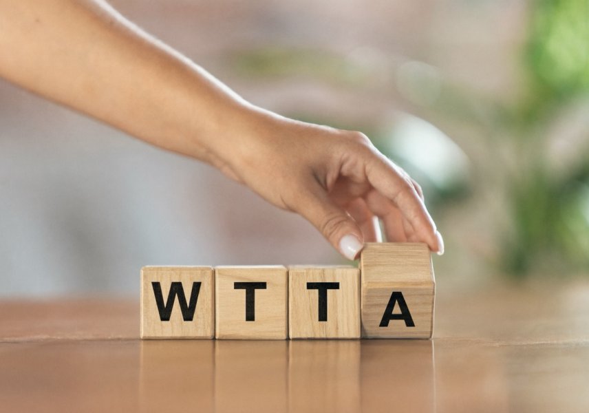 Hand legt houten blokjes met de letters WTTA op tafel