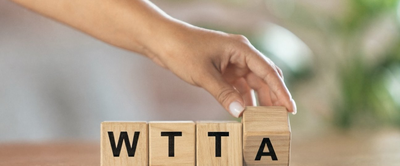 Hand legt houten blokjes met de letters WTTA op tafel